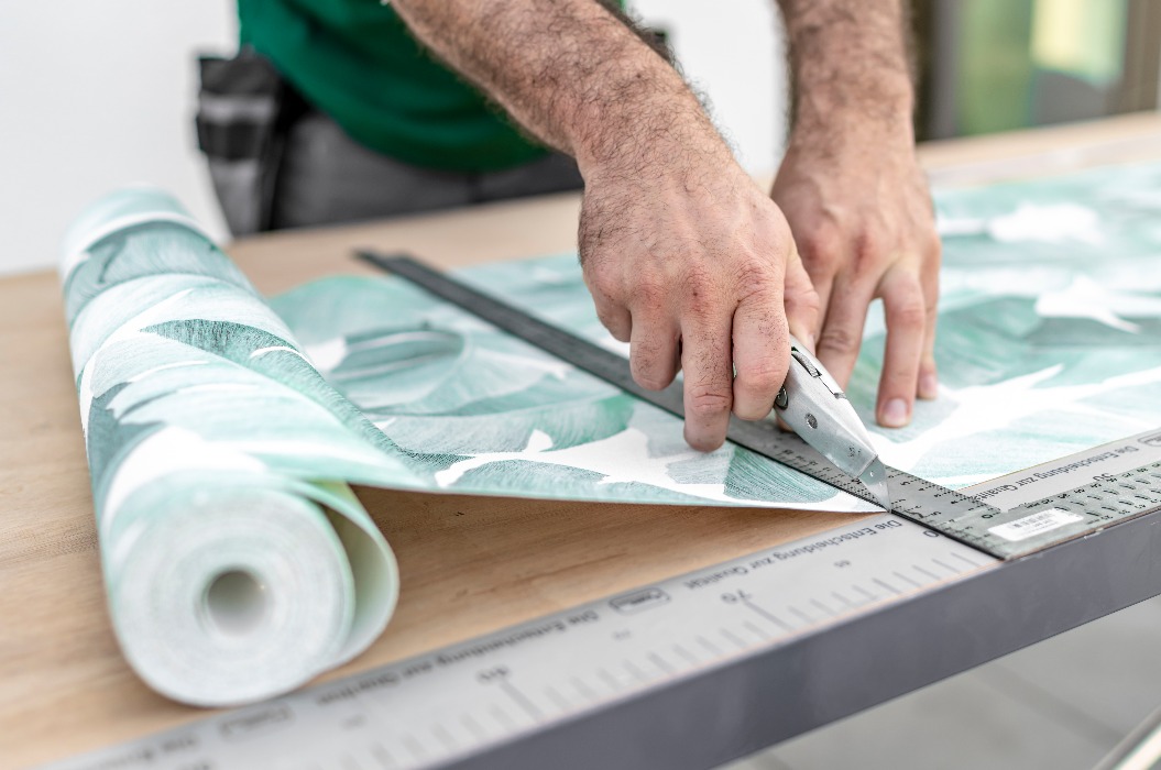 Maler schneidet die Tapete am Tapeziertisch zu