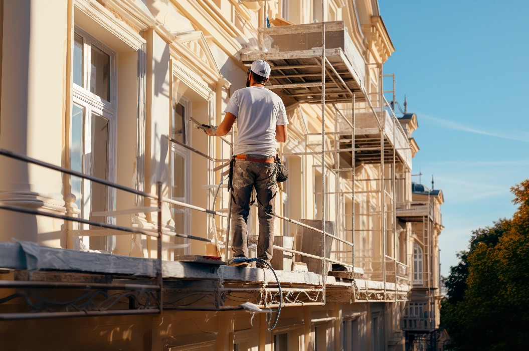 Renovierung, Restaurierung, Sanierung. Unbekannter Arbeiter renoviert die Wand eines Gebäudes im klassischen Stil, auf einem Gerüst stehend. Bauarbeiter bereitet Hausfassade für Anstrich im Freien vor